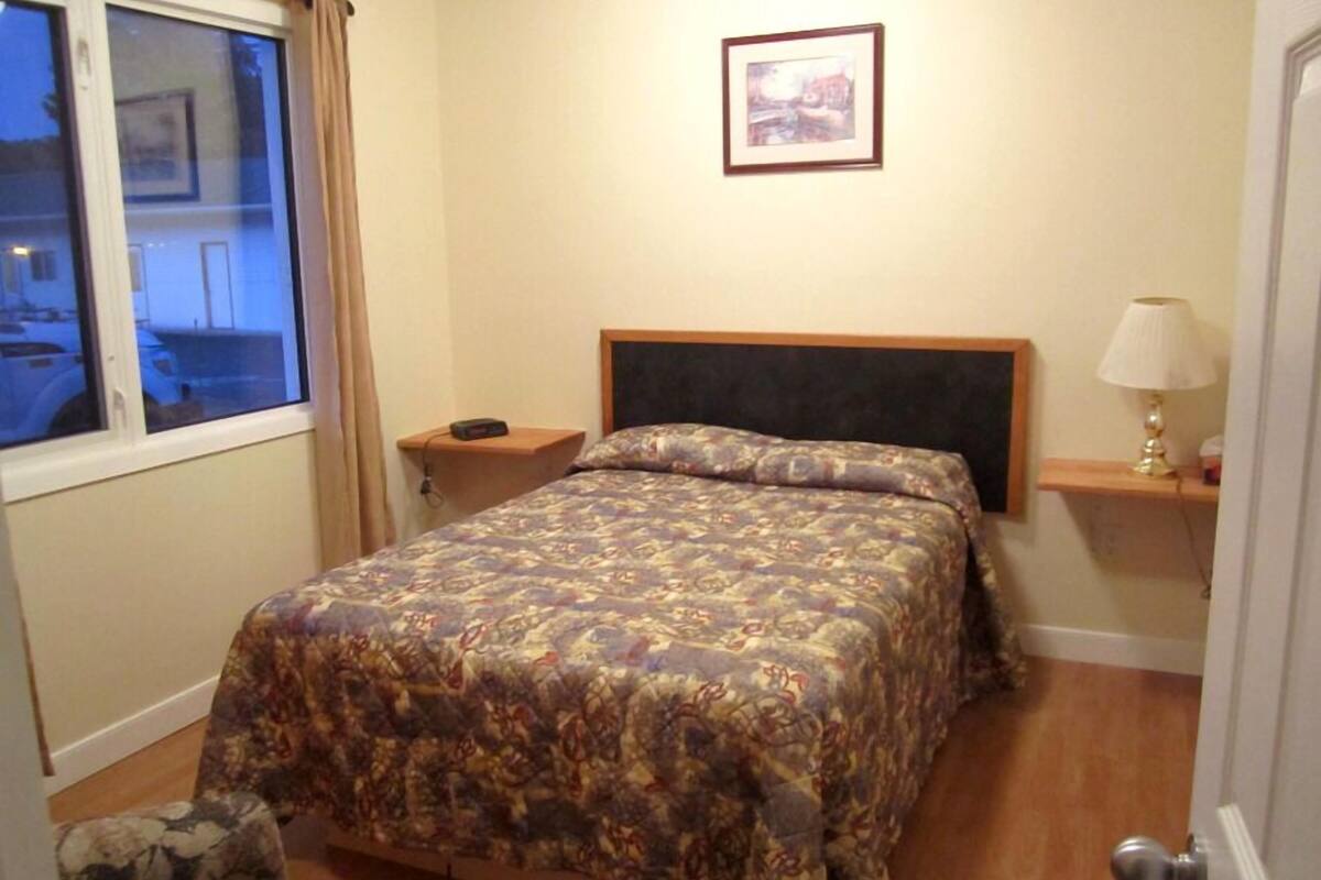 A bedroom with a bed, a nightstand, a lamp, and a window.