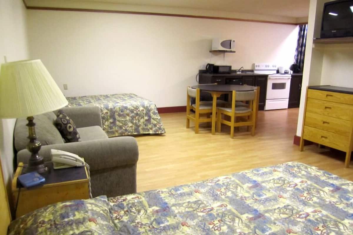 A room with two beds, a desk, a chair, a lamp, a TV, and a kitchenette.