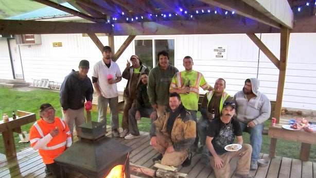 A group of people gathered around a wood-burning stove on a wooden deck with a covered area overhead, possibly for shelter. - Gateway Motel (Minnedosa)