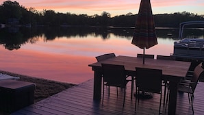 Une terrasse en bois avec une table et des chaises, un parasol et un bateau amarré au bord de l’eau.