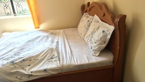 A single bed with a floral bedspread and matching pillows, a wooden headboard, and a view of the outdoors through a window with a metal railing.