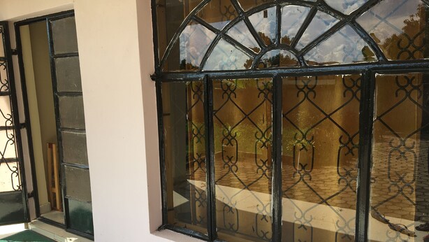 A room with a large window featuring a black metal grill, a green mat at the entrance, and a tiled floor.