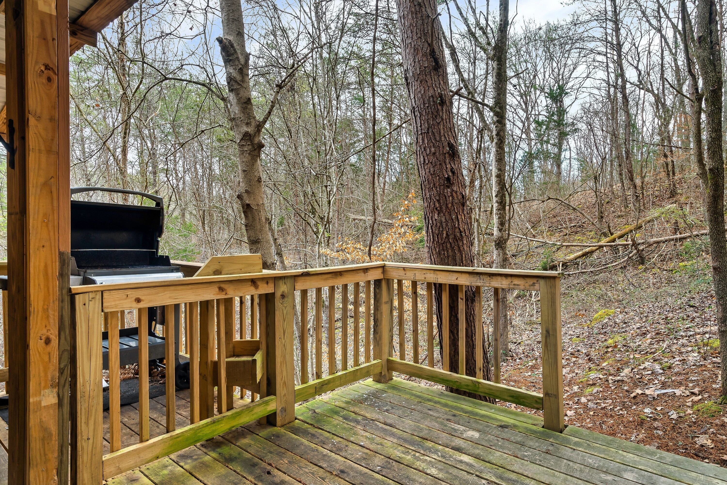 A wooden deck with a grill and seating area overlooking a forested area.