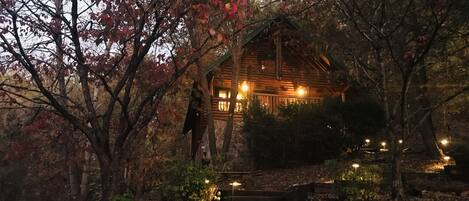 A rustic cabin with a stone foundation, surrounded by autumn foliage.