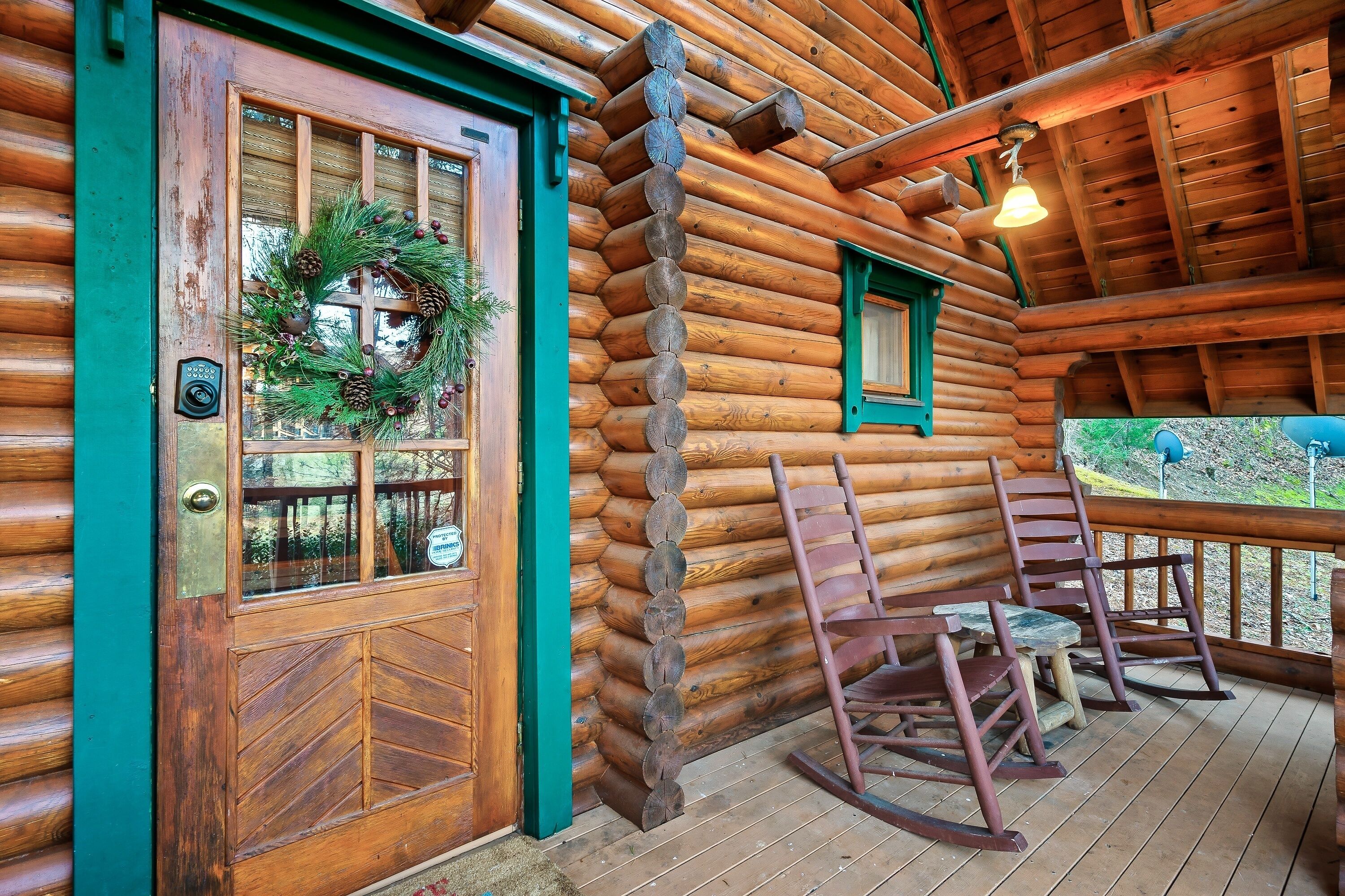 A log cabin with a wooden door, a porch with rocking chairs, and a green window frame.