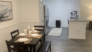 A dining area with a table set for four, a refrigerator, and a kitchen in the background. - Fabulous Fully-Furnished Apartment in Alpharetta (Alpharetta)