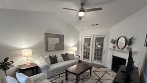 A living room with a white sofa, a coffee table, a lamp, a TV, and a fireplace. - Fabulous Fully-Furnished Apartment in Alpharetta (Alpharetta)