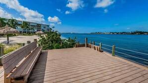 Eine Holzterrasse mit einer Bank, mit Blick auf einen Strand und einen wolkenlosen, blauen Himmel über dem Meer.