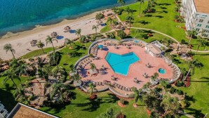 Eine Luftaufnahme eines Resorts mit einem zentralen Swimmingpool, einem Strand und Palmen.