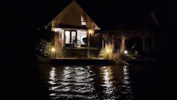 A house with a lit entrance and a pond in front. - Luxury Holiday Home, Large Garden, Free Motorboat Usage for Our Guests (Medemblik)