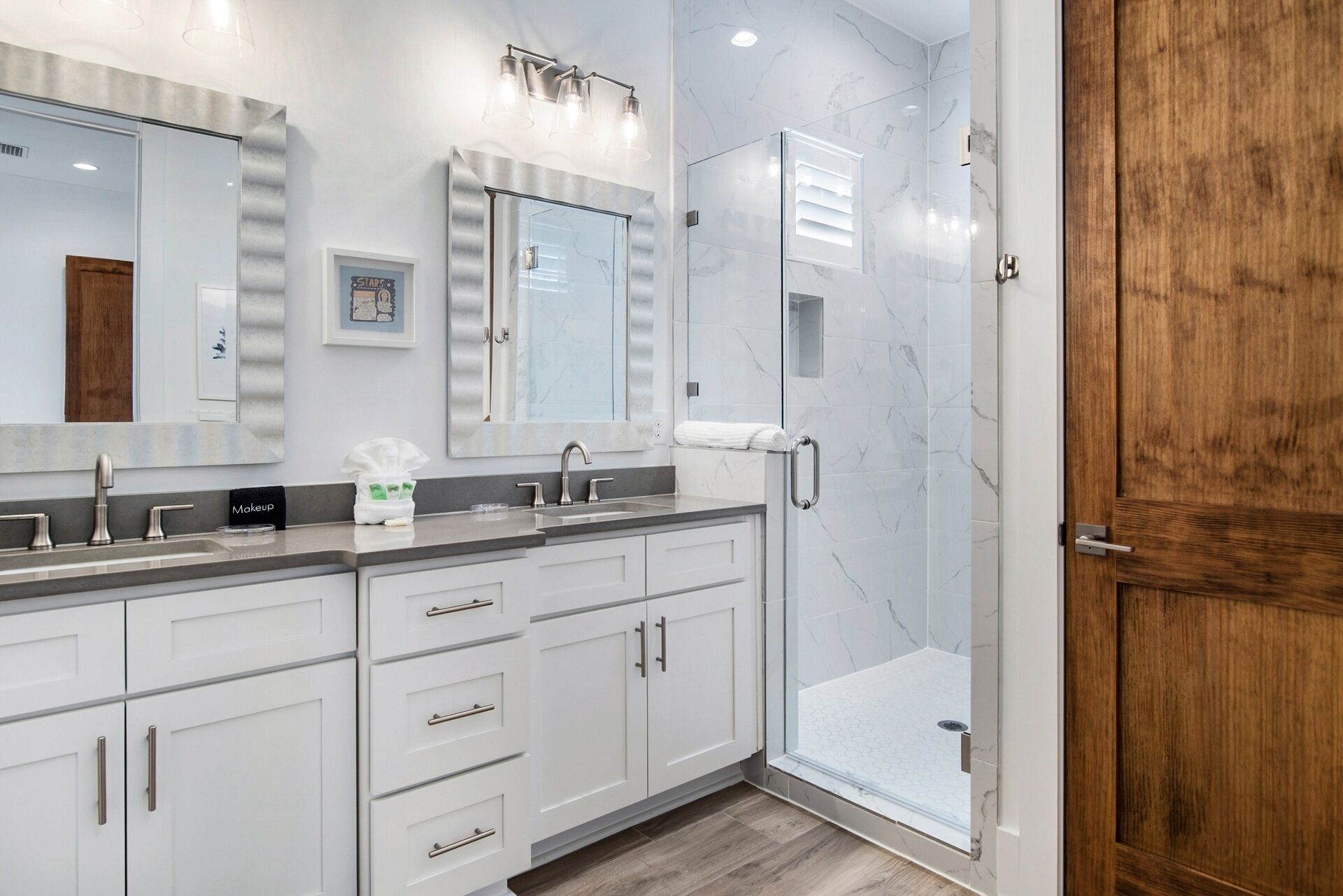 Une salle de bain moderne avec une douche à parois de verre, un meuble-lavabo doté d’un grand miroir et une porte en bois.