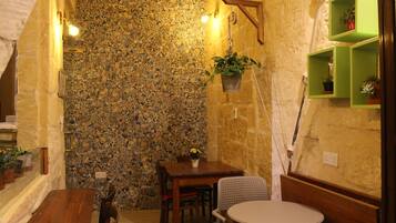 A cozy dining area with a stone wall, wooden furniture, and green shelves with plants.