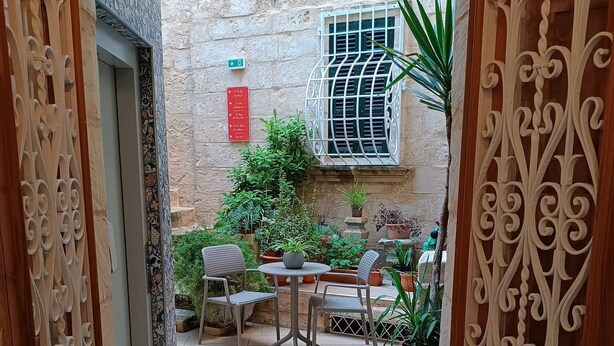 An open wooden door leading to a courtyard with a table and chairs, potted plants, and a stone wall. - Palazzino Nina Boutique Hotel (Qormi)