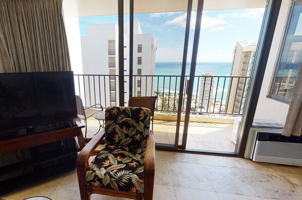 Ein Balkon mit Blick auf Strand und Meer, einem Fernseher und einem Sessel mit tropischem Muster.