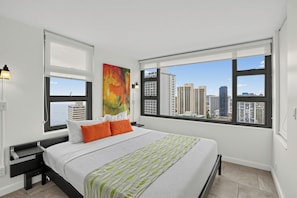 A modern bedroom with a large bed, two windows, and a city view.