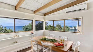 A dining area with a wooden table, white chairs, and a view of the ocean through large windows. - Sunshine Beach Shack - Pet Friendly close to the beach (Sunshine Beach)