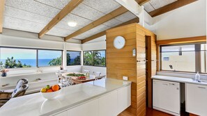 Une cuisine moderne dotée d’un grand îlot central, de touches de bois et offrant une vue sur l’océan.