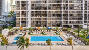 A multi-story hotel with a rooftop pool, sun loungers, and a parking area.