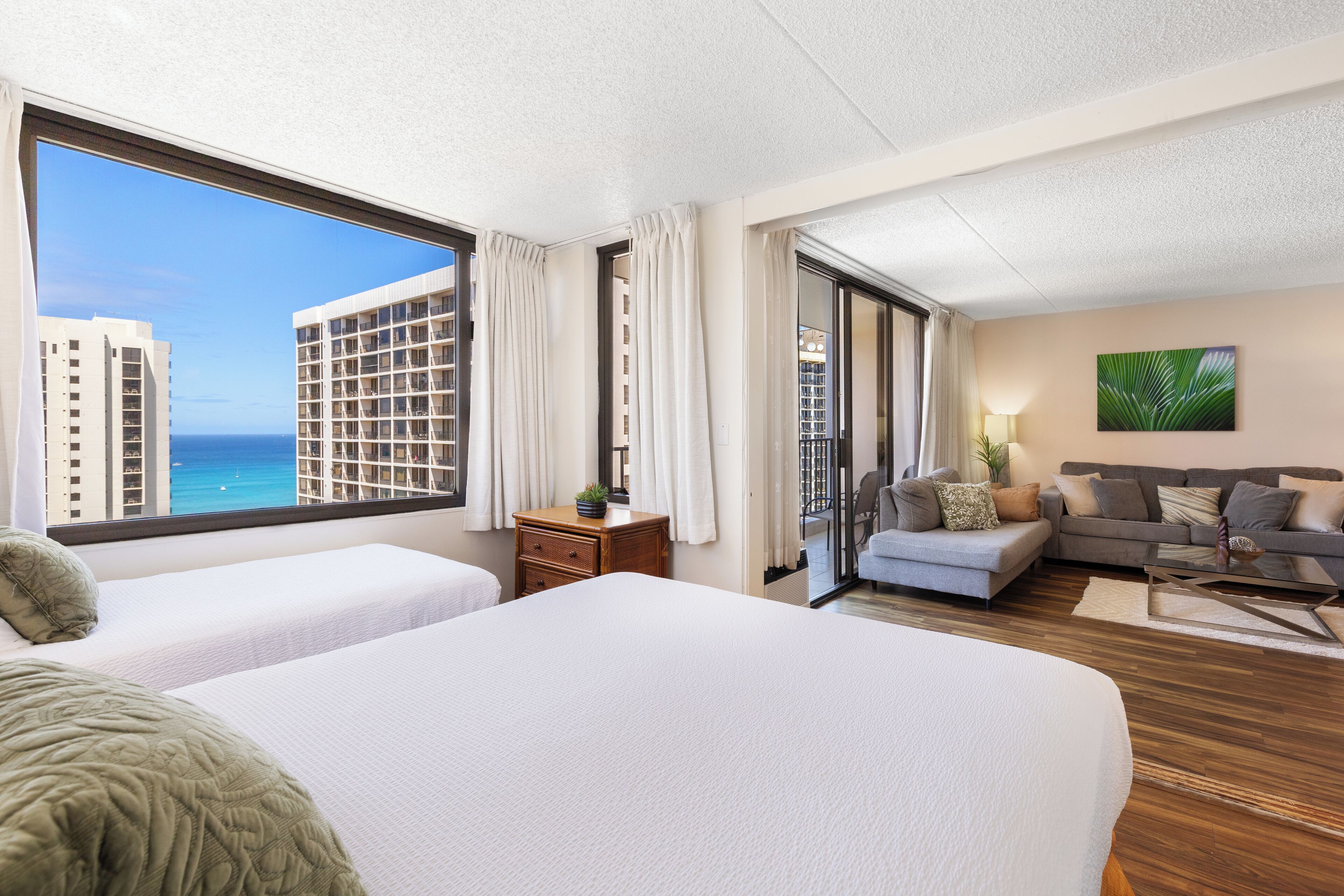 Een hotelkamer met twee bedden, een bank, een bijzettafeltje en uitzicht op de oceaan.