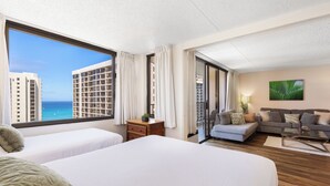 A hotel room with two beds, a sofa, a coffee table, and a view of the ocean.