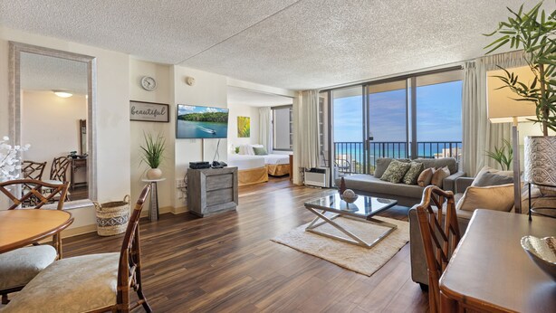 A spacious living area with a dining table, chairs, a sofa, and a large window offering a view of the outdoors.