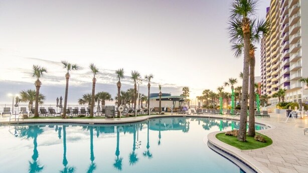 A pool area with palm trees, lounge chairs, and a high-rise building in the background.