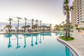 A pool area with palm trees, lounge chairs, and a high-rise building in the background.