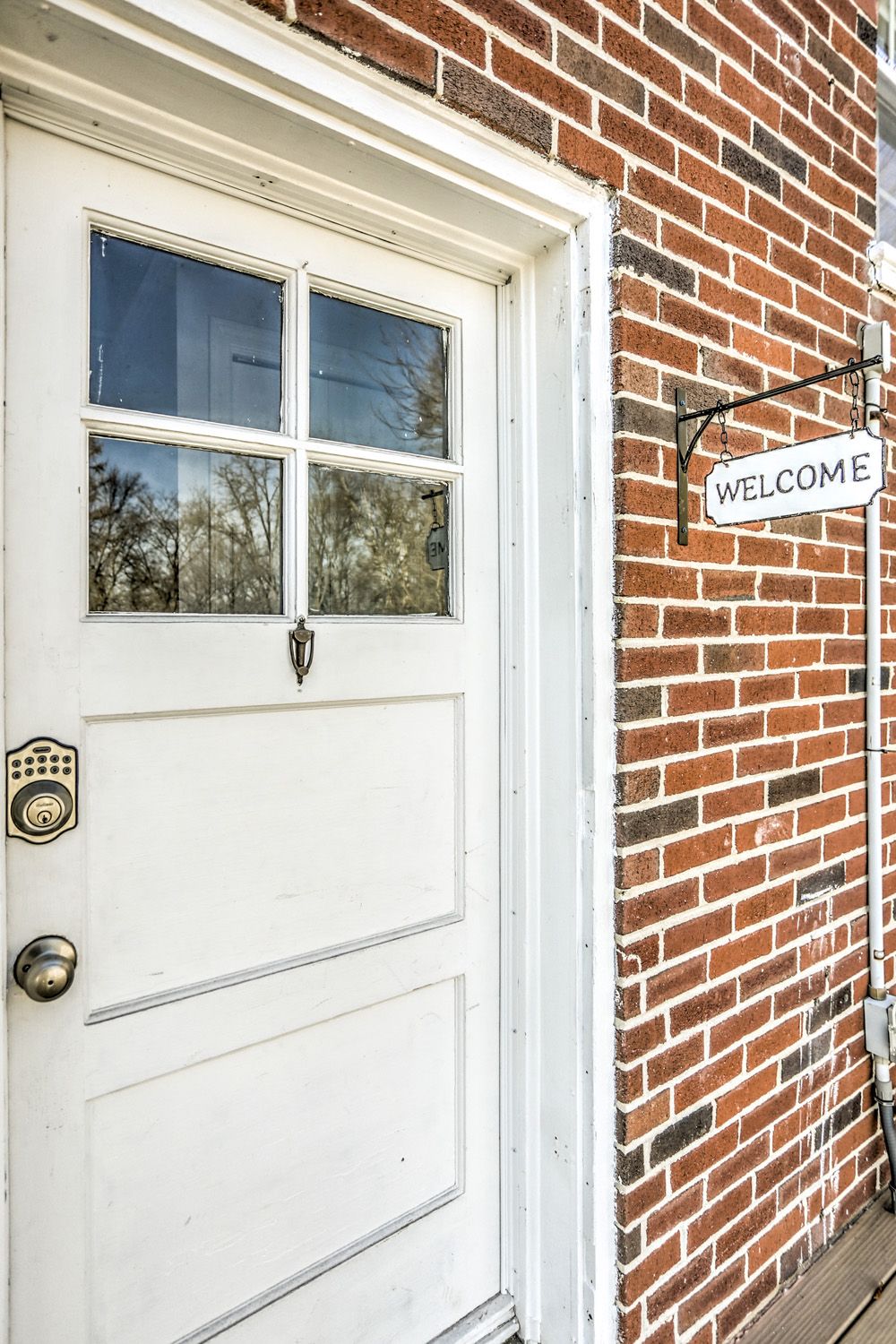 A white door with a 'WELCOME' sign on a brick wall.