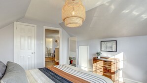 Ein Schlafzimmer mit einem großen Bett, einer Holzkommode, einer Pendelleuchte und einer Tür zu einem anderen Raum.