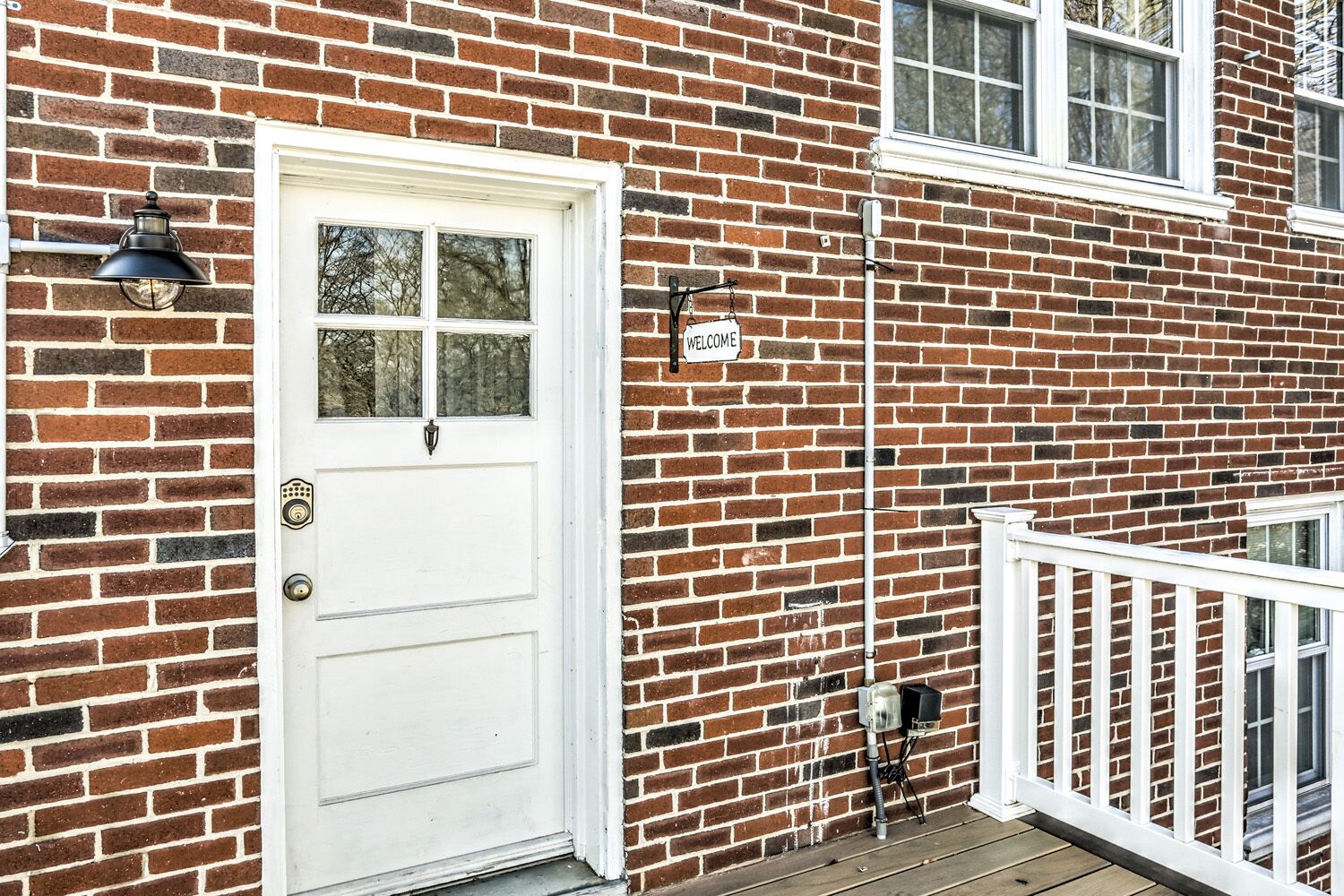 A white front door with a glass panel, a 'WELCOME' sign, and a white railing on a brick house.