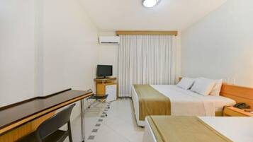 Quarto de hotel com uma cama, uma escrivaninha, uma cadeira, uma televisão e um pequeno armário.
