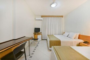 Una habitación de hotel con cama, escritorio, silla, televisor y un pequeño armario.