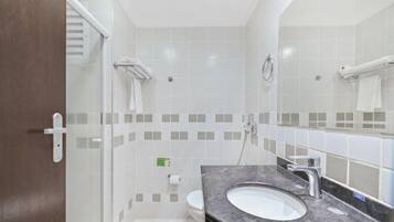 Un baño moderno con cabina de ducha de vidrio, un lavabo blanco con encimera de mármol y un espejo grande.