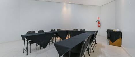 Un salón de conferencias con una larga mesa, sillas y un pequeño atril cubierto con un mantel negro.