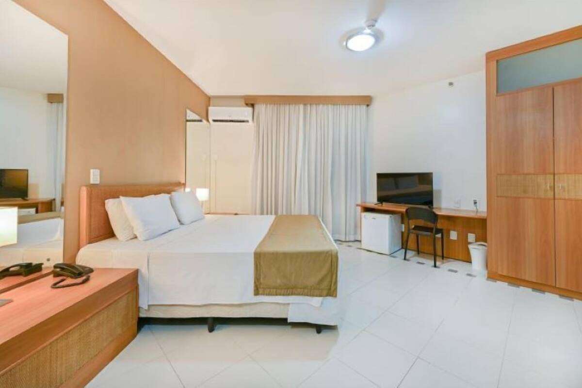 A hotel room with a bed, desk, chair, and a wardrobe.