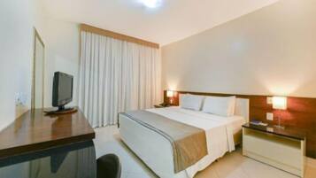 Una habitación de hotel con una cama, mesitas de noche, un escritorio con una computadora, un televisor y cortinas.