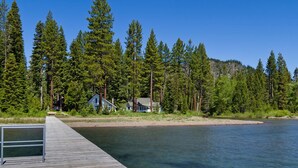 Une jetée en bois s’étendant dans un lac paisible, entourée d’une forêt verdoyante et dense, ainsi que de quelques maisons.