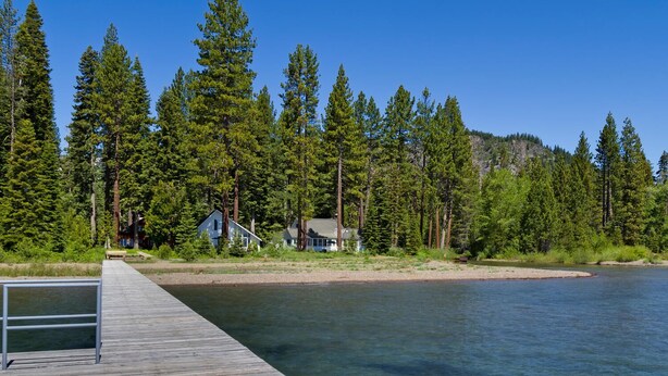 A wooden dock extending into a calm lake, surrounded by dense green forest and a few houses. - Belleview Lakefront by Tahoe Getaways - Hot Tub, Pier, Buoy and Guest House (Homewood)