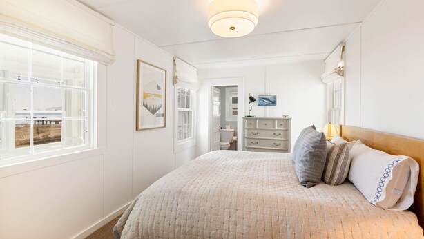 Une chambre avec un grand lit, une fenêtre donnant sur un beau paysage, une commode et un luminaire au plafond.