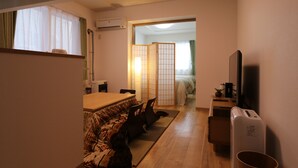 Ett kompakt hotellrum med trägolv, en säng med en grön gardin, ett litet skrivbord med en tv och en skjutdörr som leder till ett annat rum.