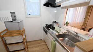 Ett kompakt kök med mikrovågsugn, spis, diskho och en torkställning i trä.