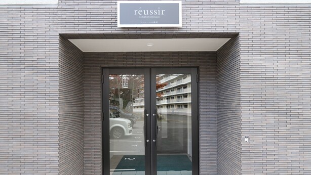 En modern entré till en byggnad med en skylt där det står ”réussir” och en glasdörr.