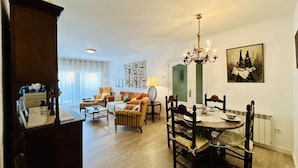 A dining area with a chandelier, a dining table with chairs, and a sofa in the background.
