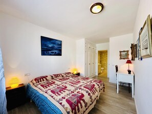 Una camera da letto con un letto, lampade da comodino, un comodino, una scrivania, una sedia, un quadro incorniciato e l'ingresso del bagno.