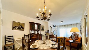 A dining area with a round wooden table, chairs, a chandelier, and a sofa.