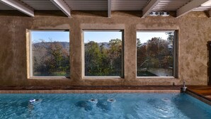Ein Schwimmbecken mit drei großen Fenstern, das Blick auf Bäume und Hügel bietet.