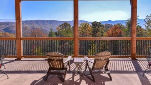 Eine Holzterrasse mit zwei Adirondack-Stühlen und einem Tisch, mit Blick auf eine gebirgige Landschaft.