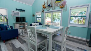 A dining area with a white table and chairs, a TV, and a blue couch. - Fish Fever, Russell Island Bahamas (Russell Island / Spanish Wells)