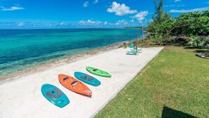 A beach with kayaks lined up on the sand, a grassy area, and a clear view of the ocean. - Fish Fever, Russell Island Bahamas (Russell Island / Spanish Wells)