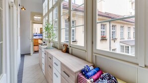 Een smalle gang met grote ramen, een houten dressoir en een plant.